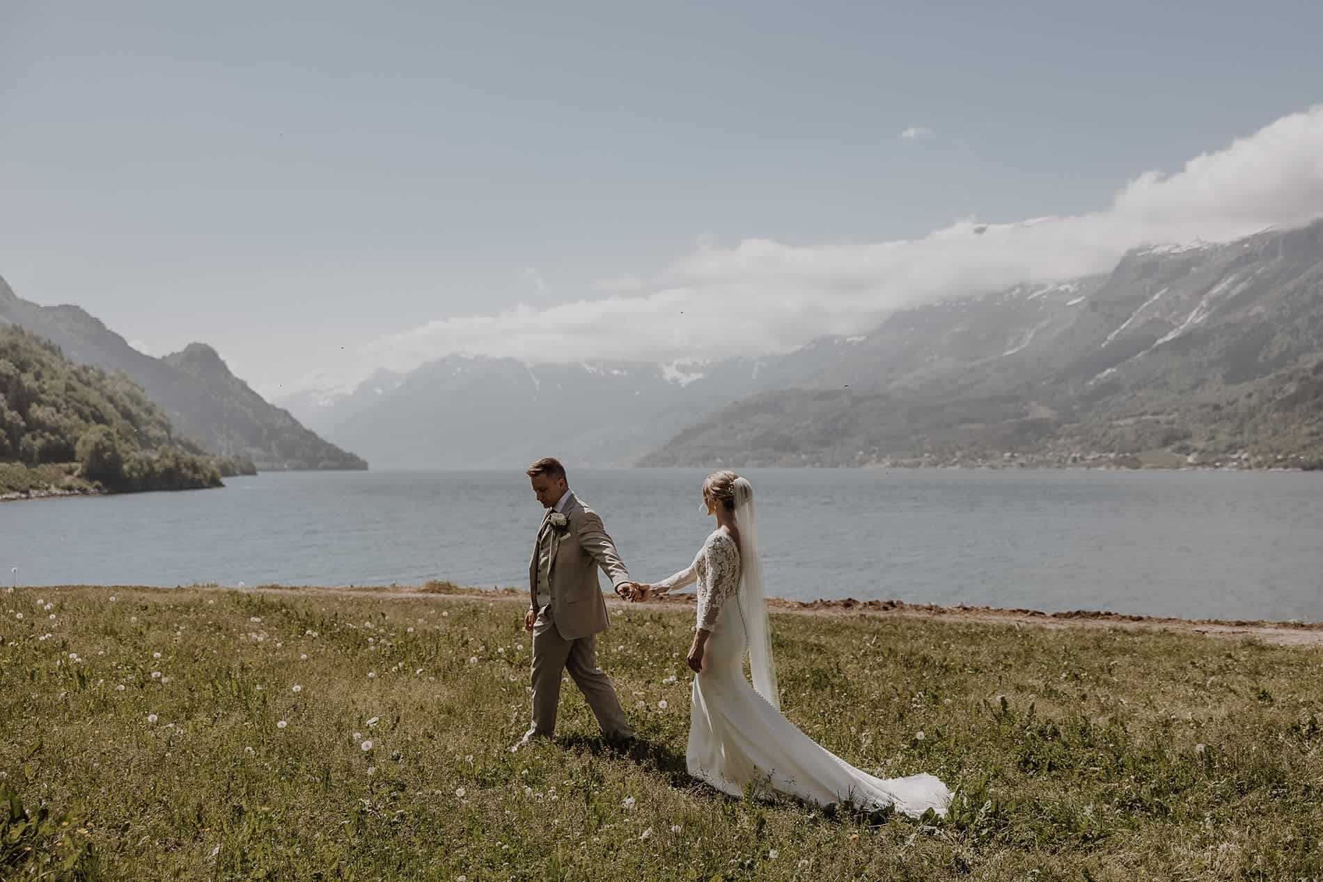 Elegant bride and groom holding hands by a scenic mountain lake during wedding workshop.