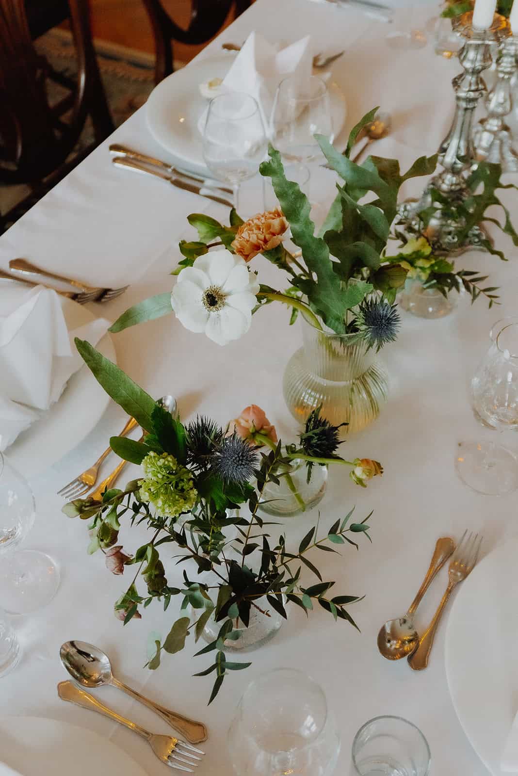 Elegant floral table centerpiece with white anemone, greenery, and candles for wedding workshop.