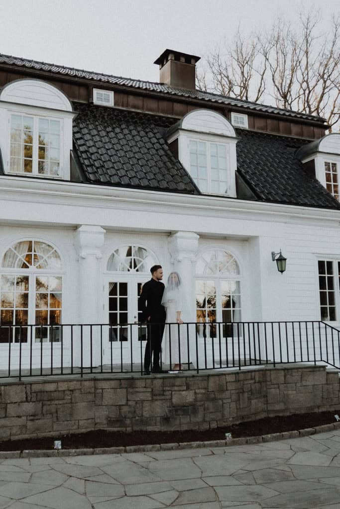 Elegant couple standing on a balcony in front of a white historic building during a wedding photogra.