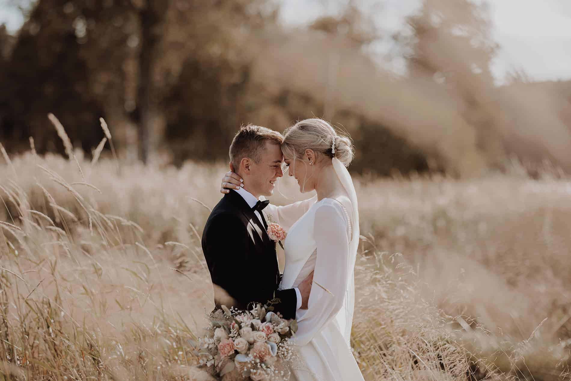 Romantic wedding photo of bride and groom in a field during sunset.