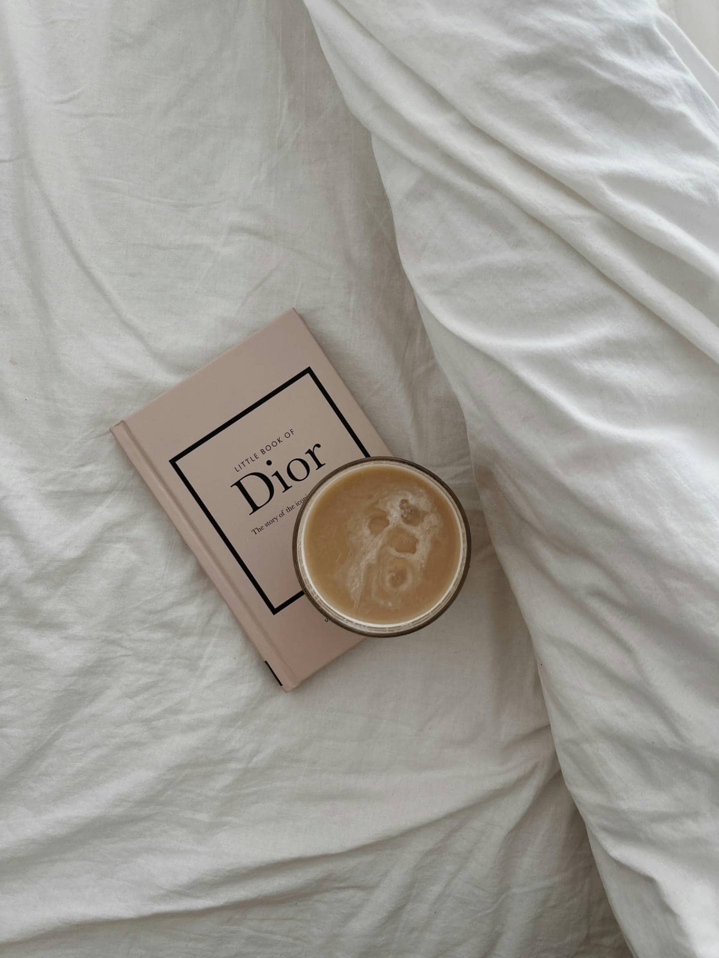 Elegant Dior book and coffee on a cozy bed, showcasing luxury lifestyle and relaxation.