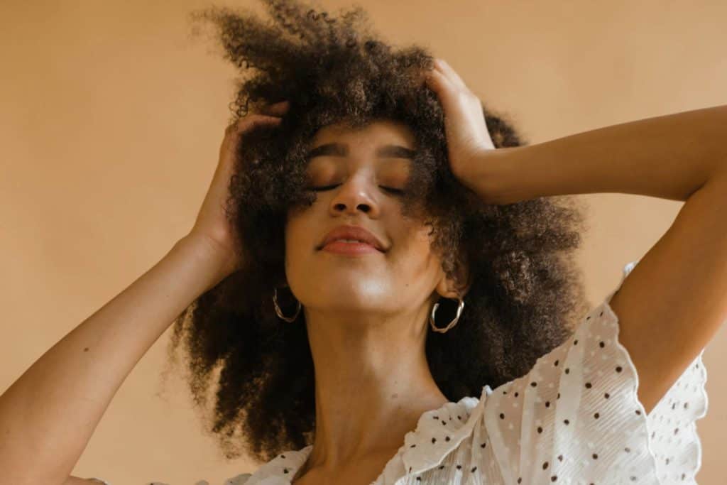 Portrait of a woman with natural curly hair, smiling softly, wearing a polka dot top.