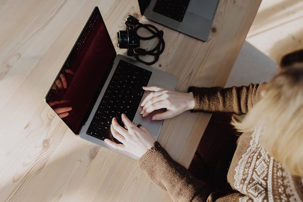 Elegant woman working on a laptop at a wooden desk, focusing on web design and digital creativity.