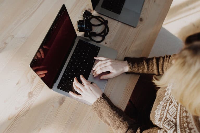 Elegant woman working on a laptop at a wooden desk, focusing on web design and digital creativity.