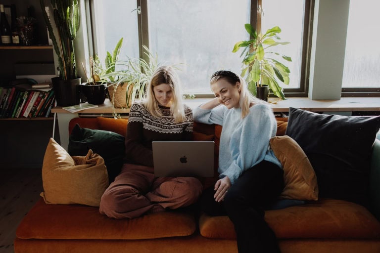 Creative women collaborating on a laptop in a cozy, plant-filled home office environment.
