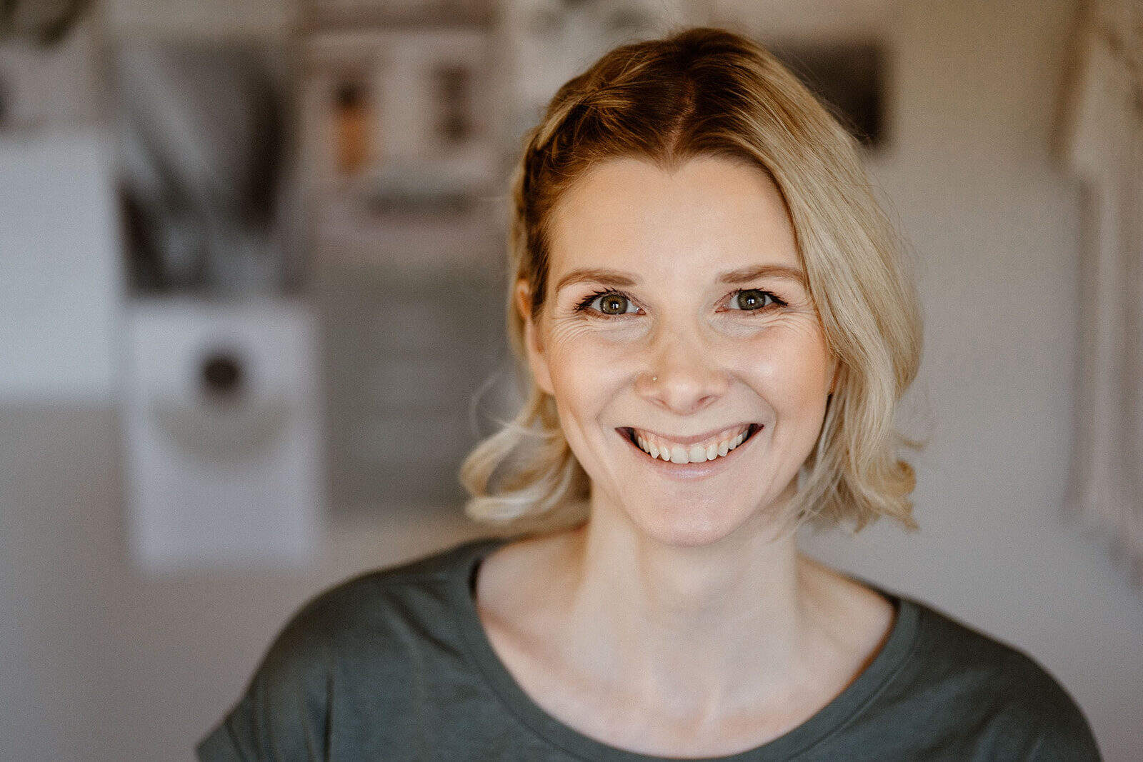 A woman with blonde hair smiling in a cozy, well-lit home environment.